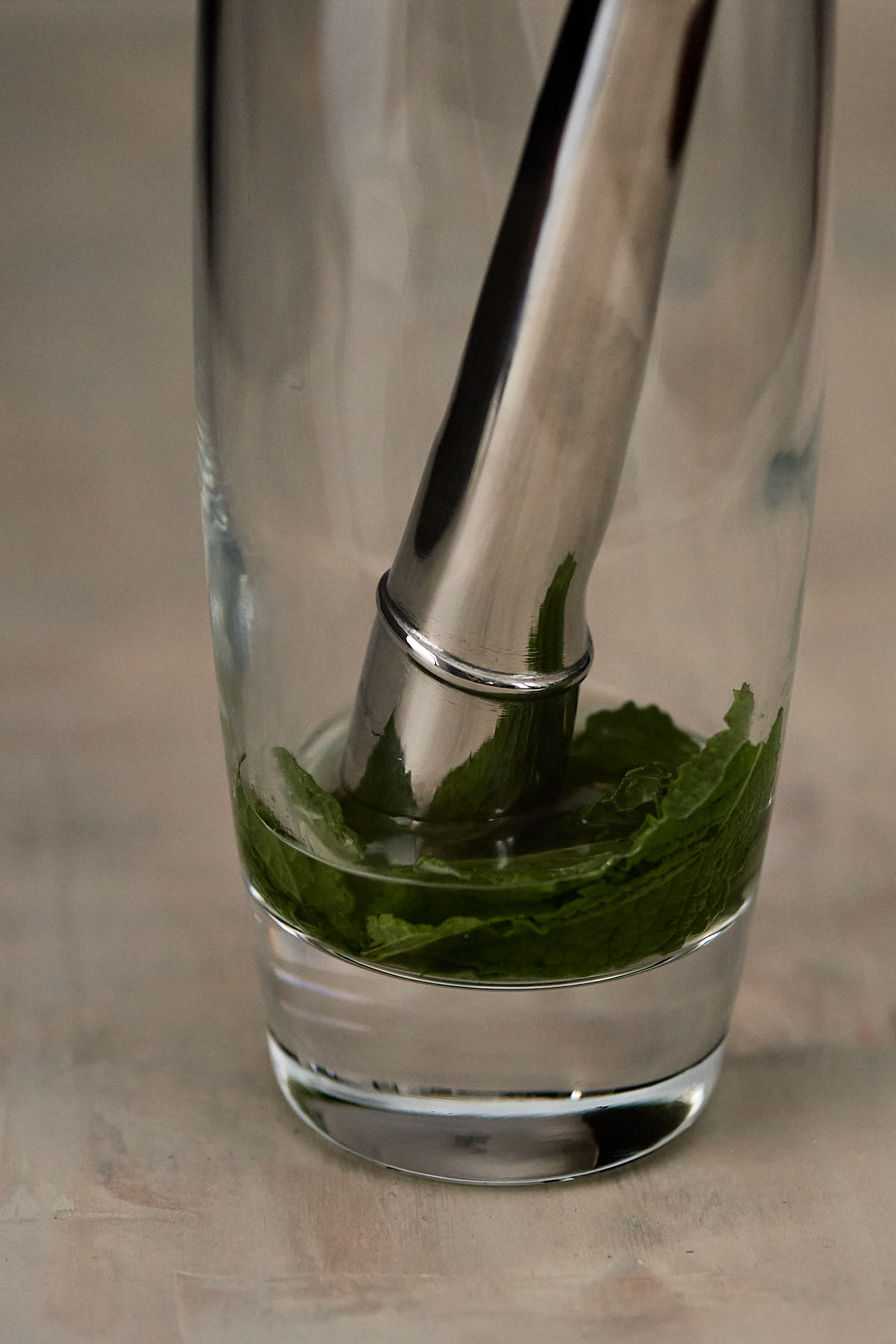 Tall glass with mint leaves and a cocktail muddler