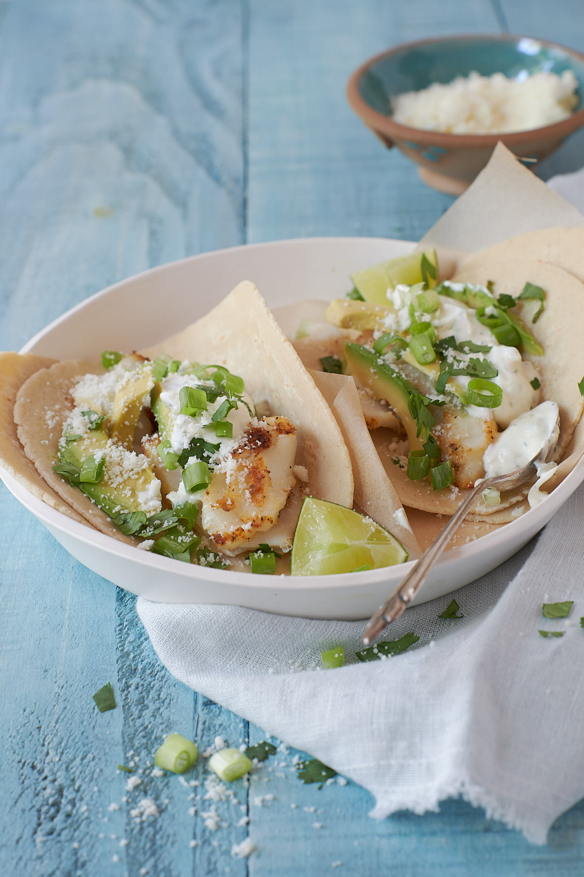 Two grilled fish tacos topped with sauce and avocado in a off white bowl