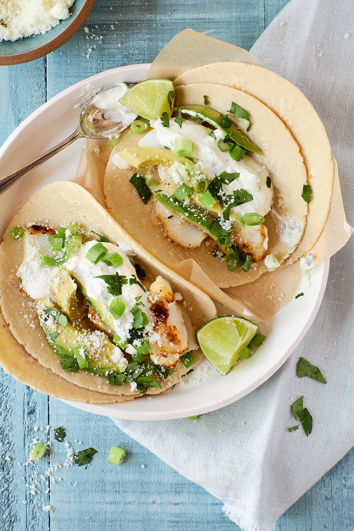 Overhead shot of two fish tacos with avocado and lime wedges on the side