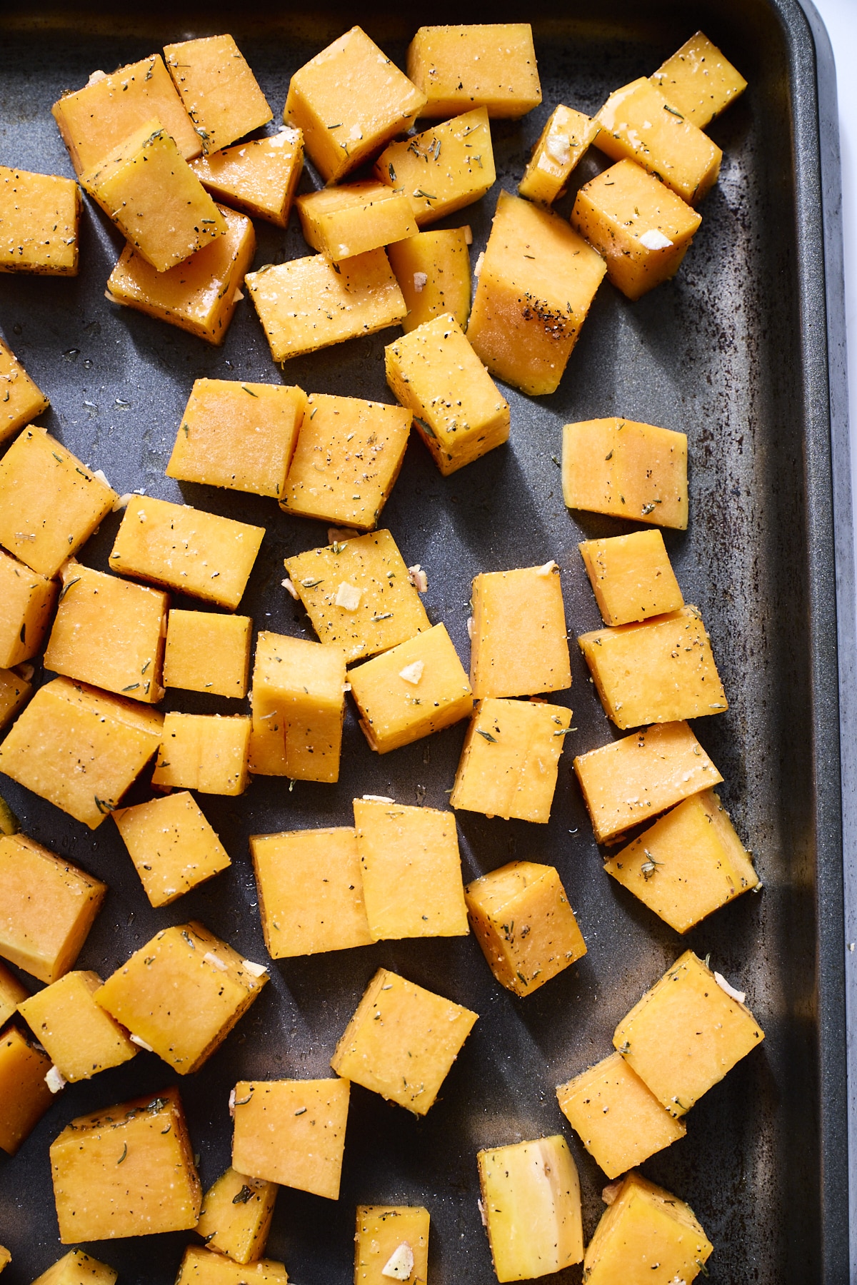 Cubed butternut squash on a dark sheet pan