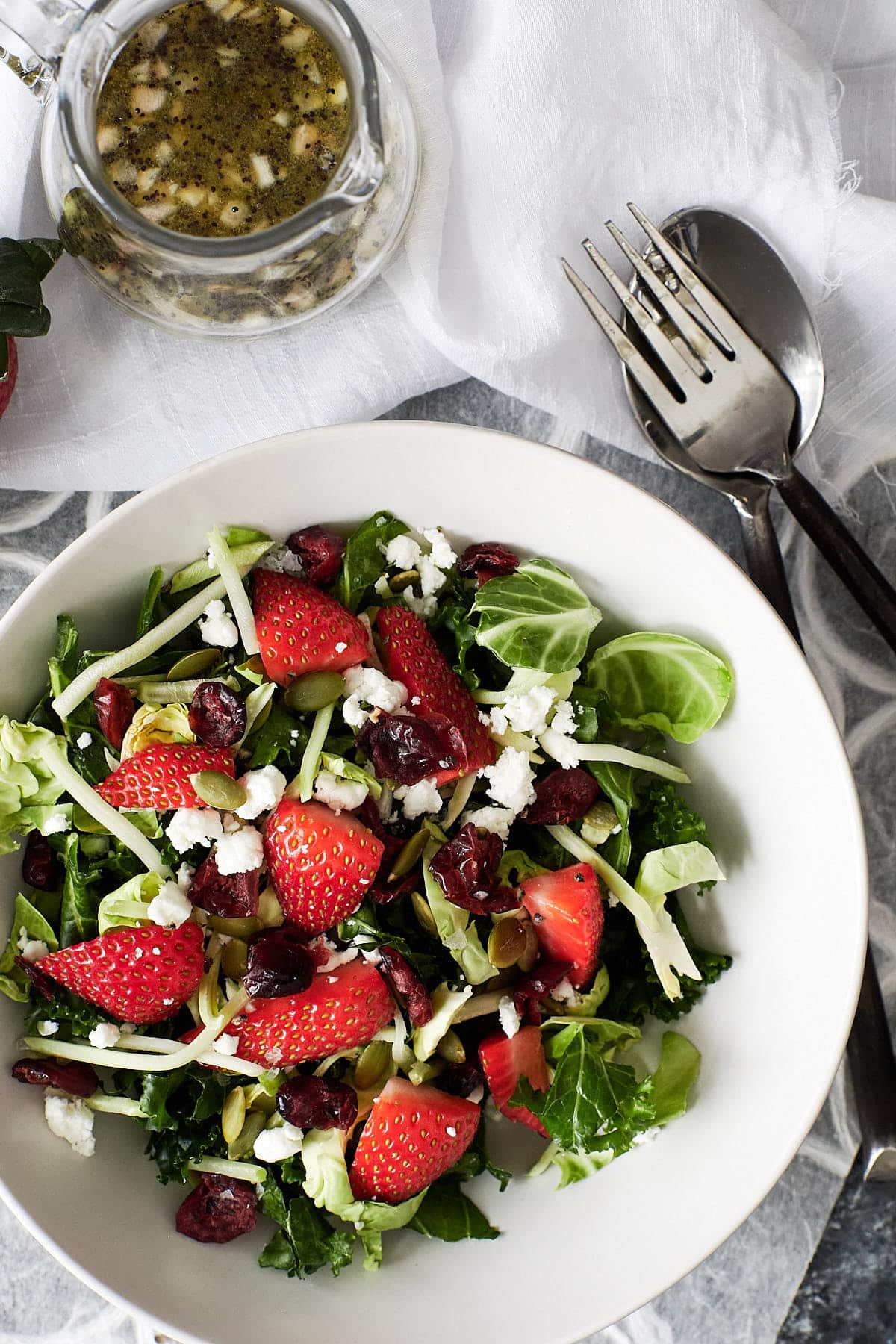 Overhead shot of kale salad topped with brussels sprouts, strawberries, goat cheese and dried cranberries