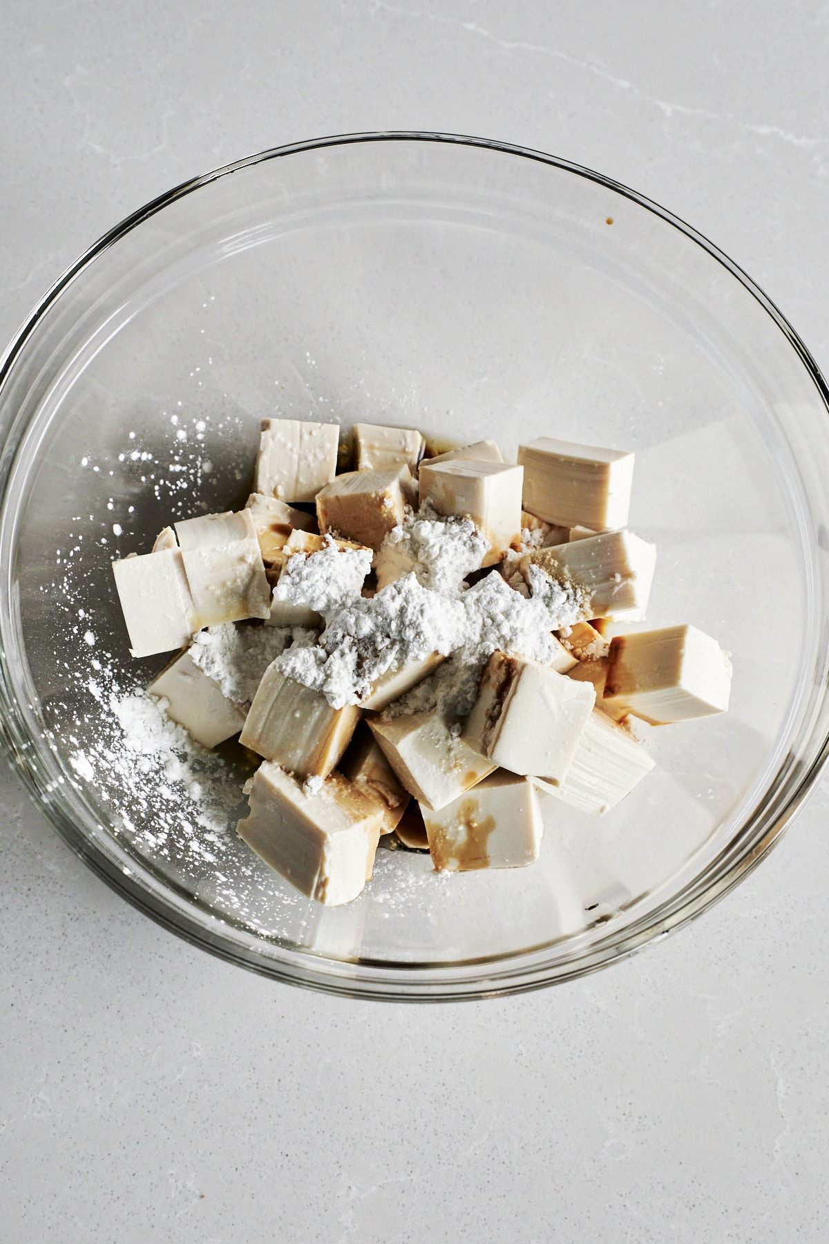 Cubes of tofu in a mixing bowl topped with cornstarch
