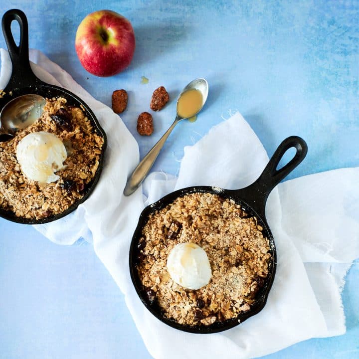 Small black cast iron skillet filled wtih an apple crisp topped with a scoop of ice cream