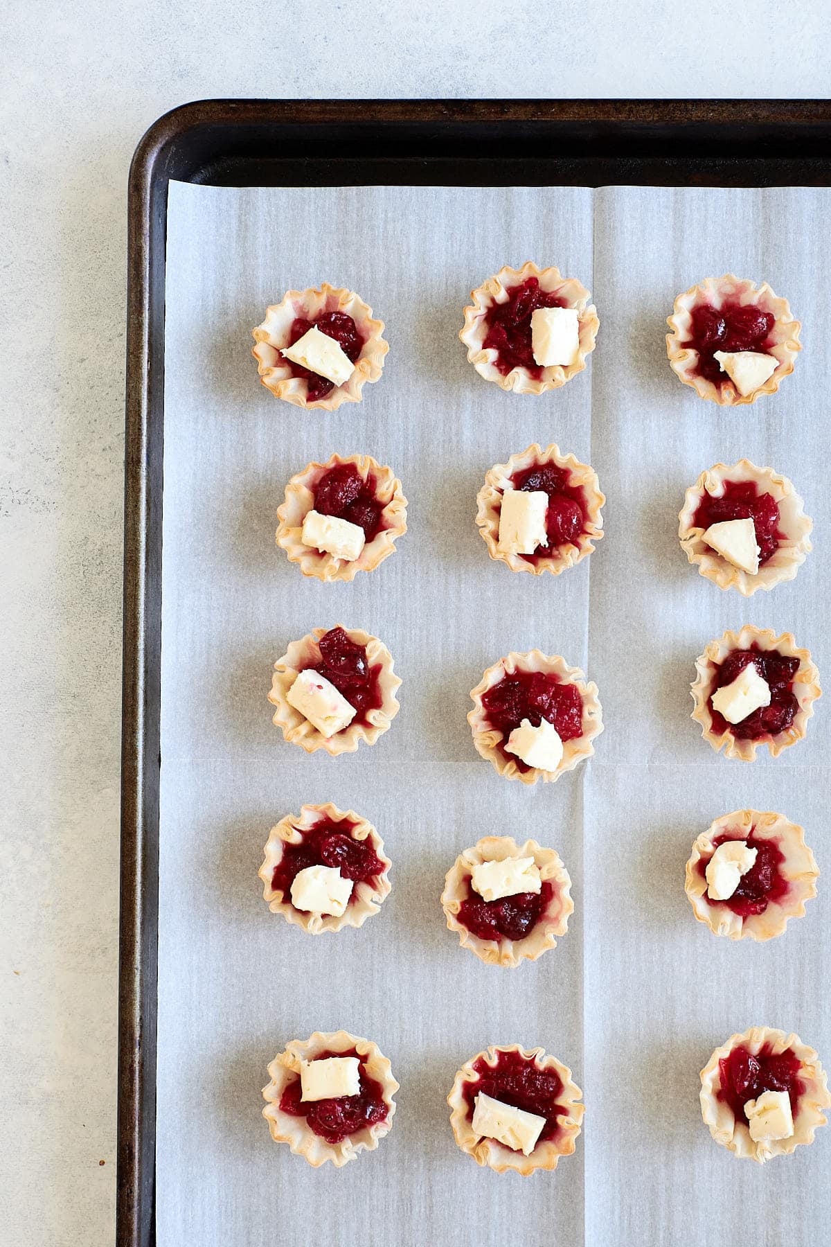 Uncooked cranberry brie mini tarts on a baking sheet