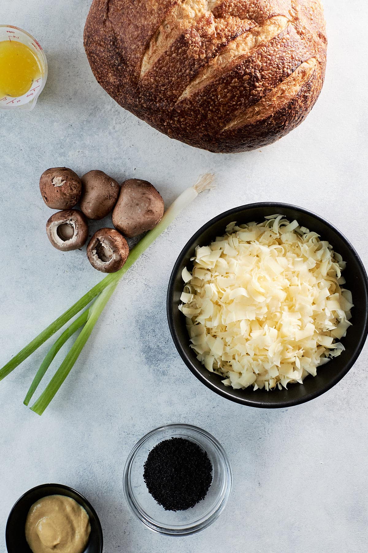 Ingredients for pull-apart bread - sourdough round, mushrooms, green onions, shredded swiss cheese, mustard and poppy seeds