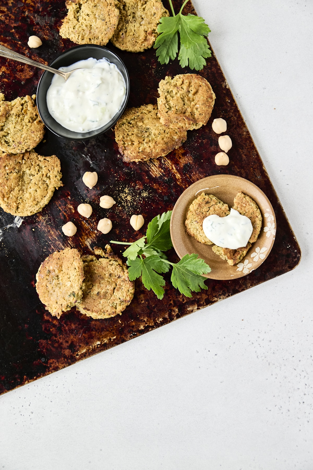 Falafel patties on a dark baking sheet with a small bowl of tzatziki sauce