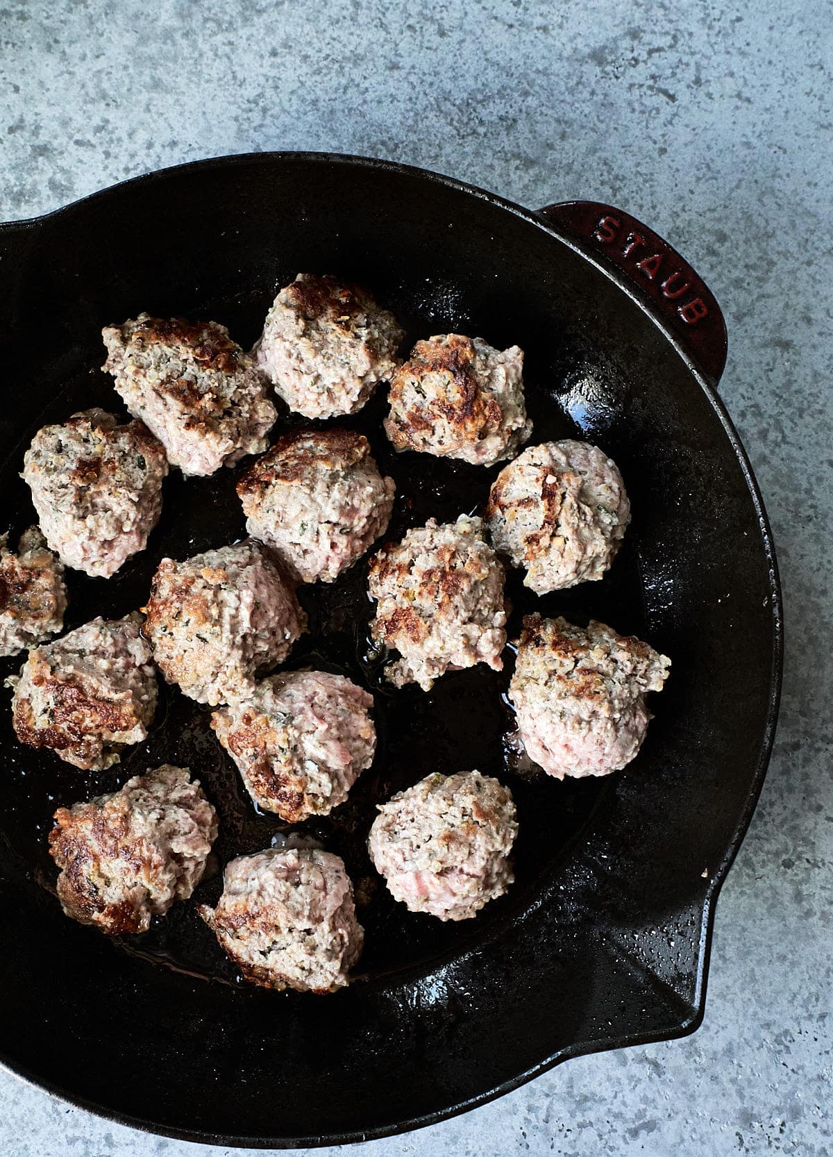 Meatballs being browned in a cast iron skillet