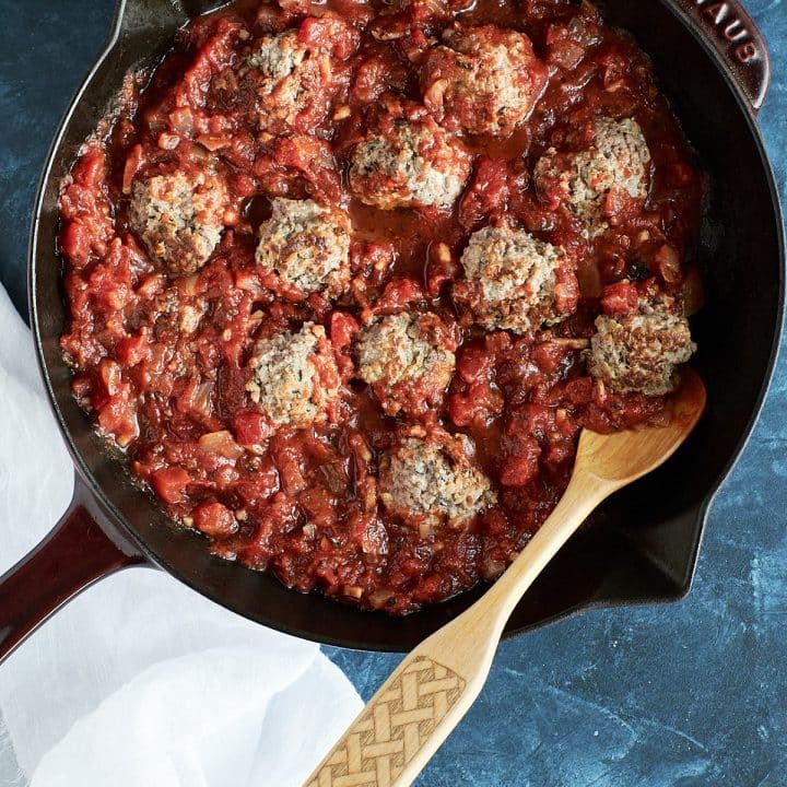 Meatballs made with ricotta and ground beef, topped with red sauce in a sauté pan.