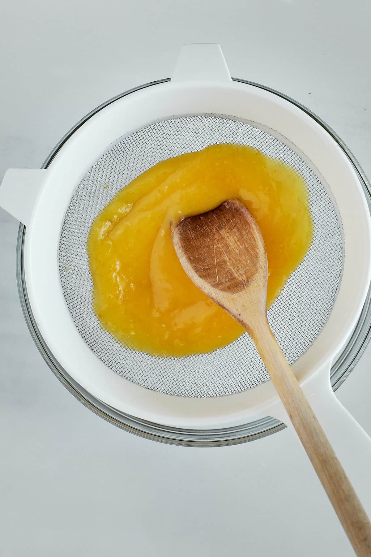 Cooked lemon curd being pushed through a fine strainer