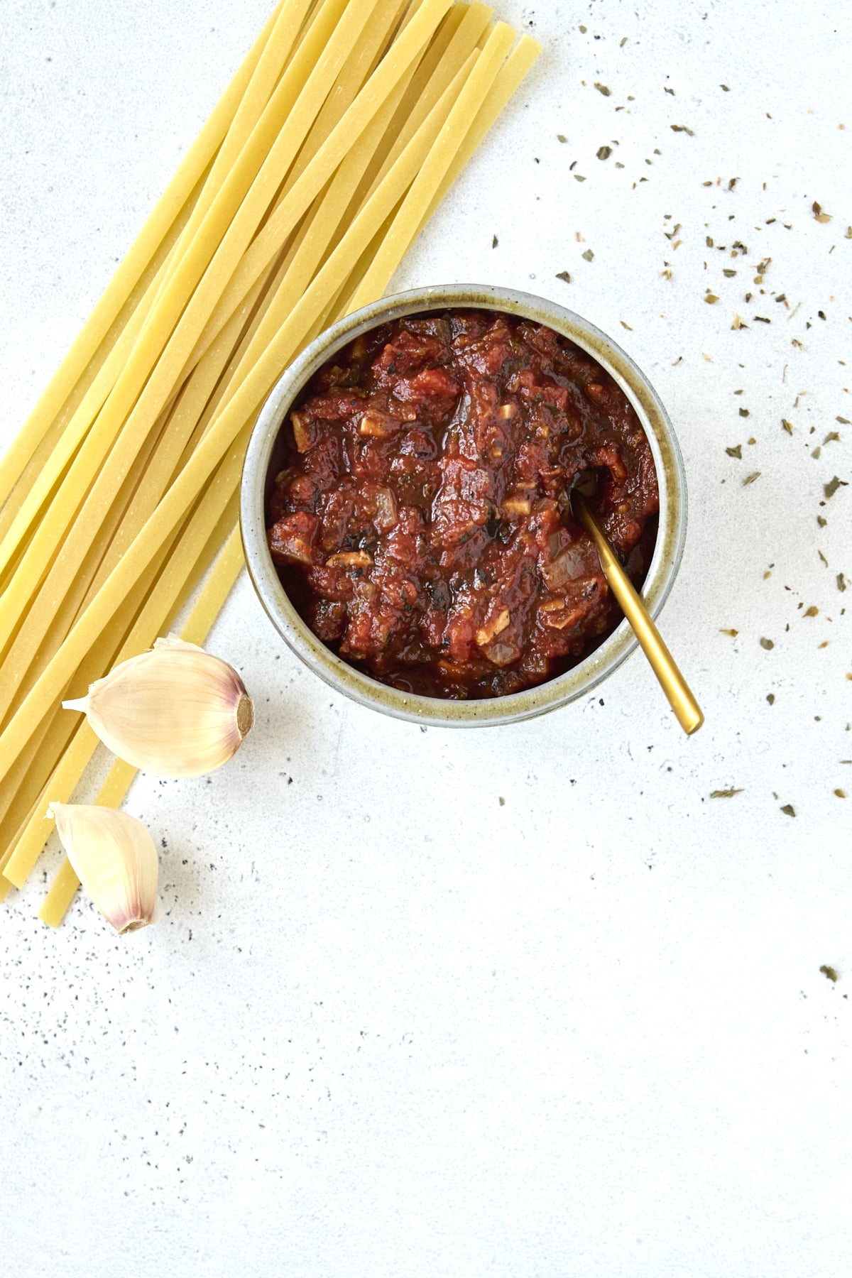 Small bowl of tomato sauce with uncooked pasta noodles on the side