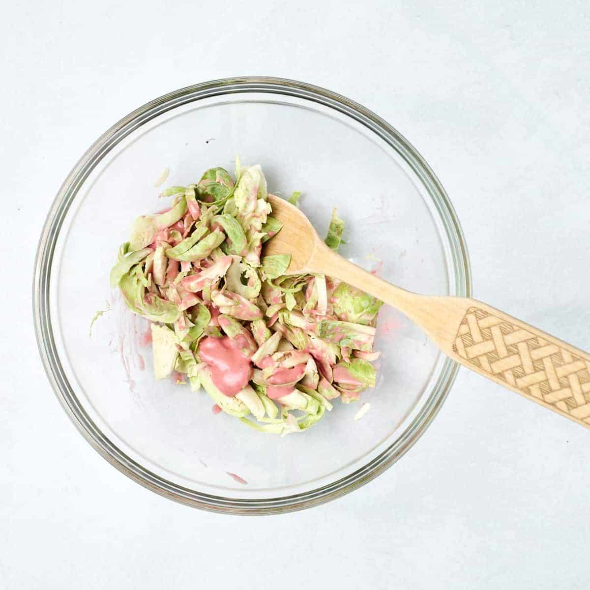 Sliced brussels sprouts and raspberry dressing mixed in a glass bowl