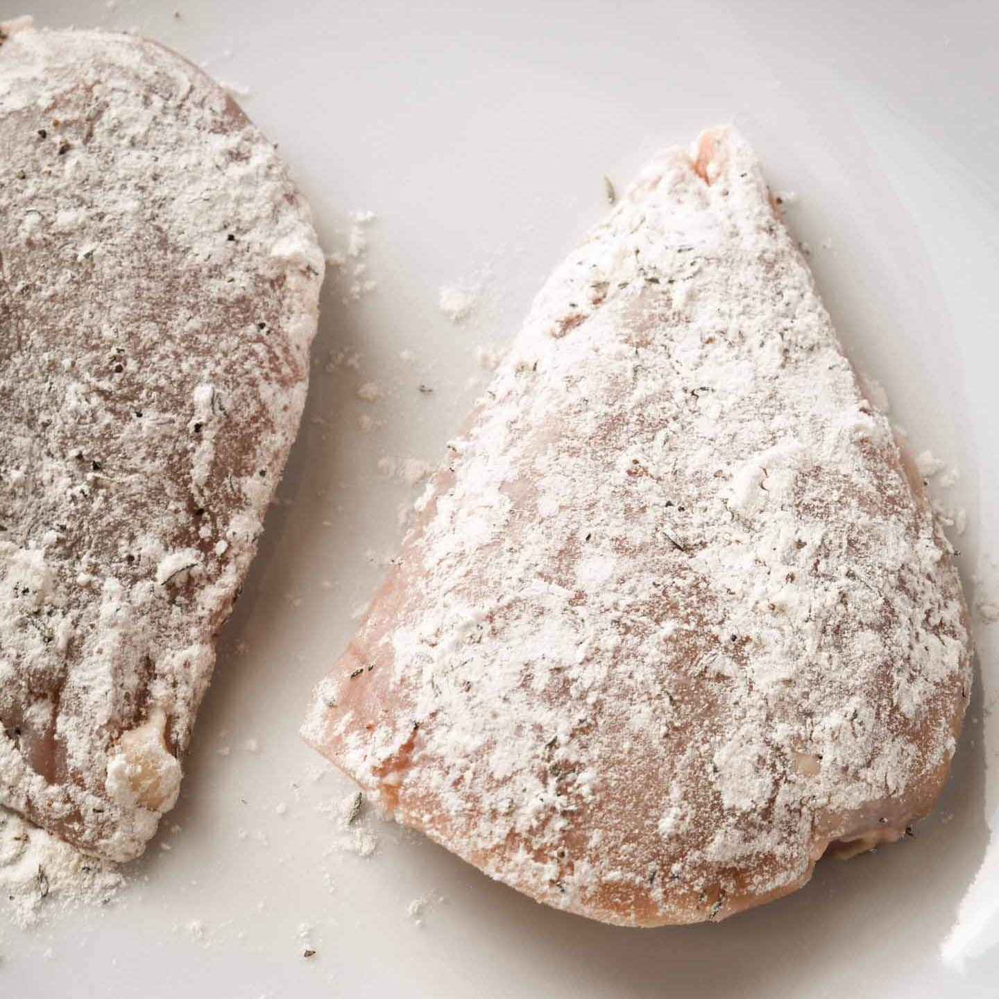 Floured chicken breasts on a white plate
