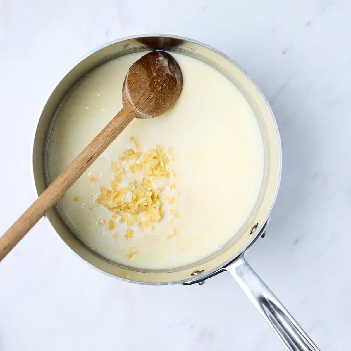 Grated cheese added to roux mixture in a stainless steel sauce pan