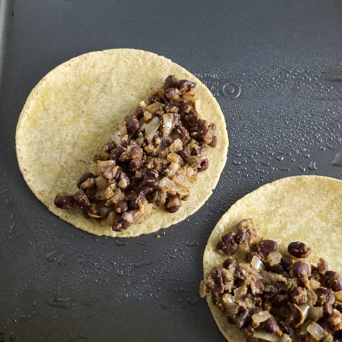 Corn tortillas on a baking sheet with black bean taco filling spread on half