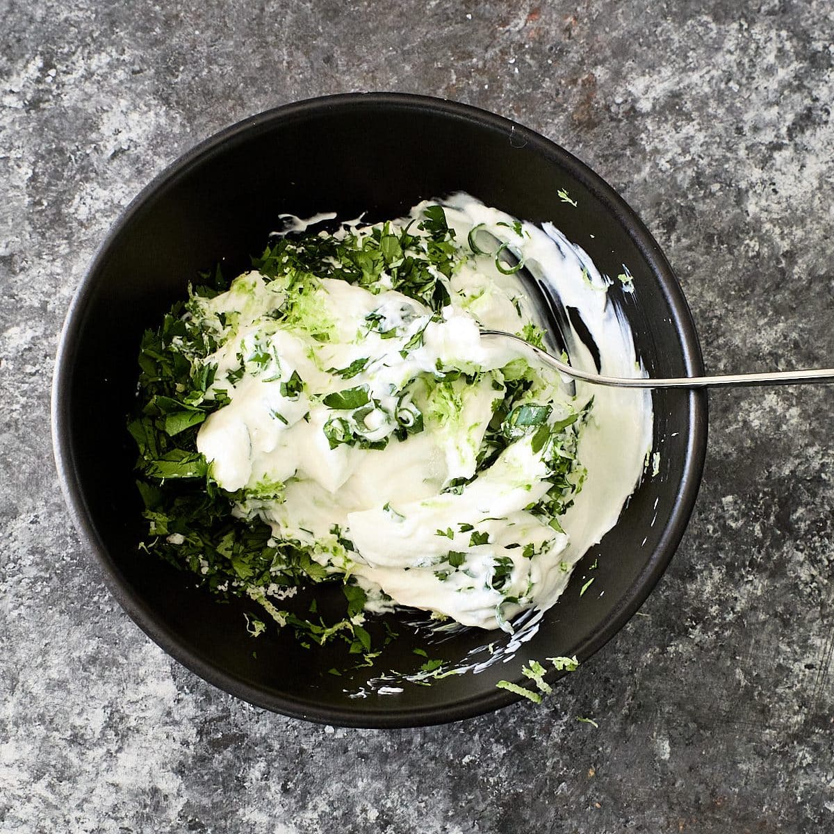 Greek yogurt, cilantro and lime juice being mixed in a dark bowl
