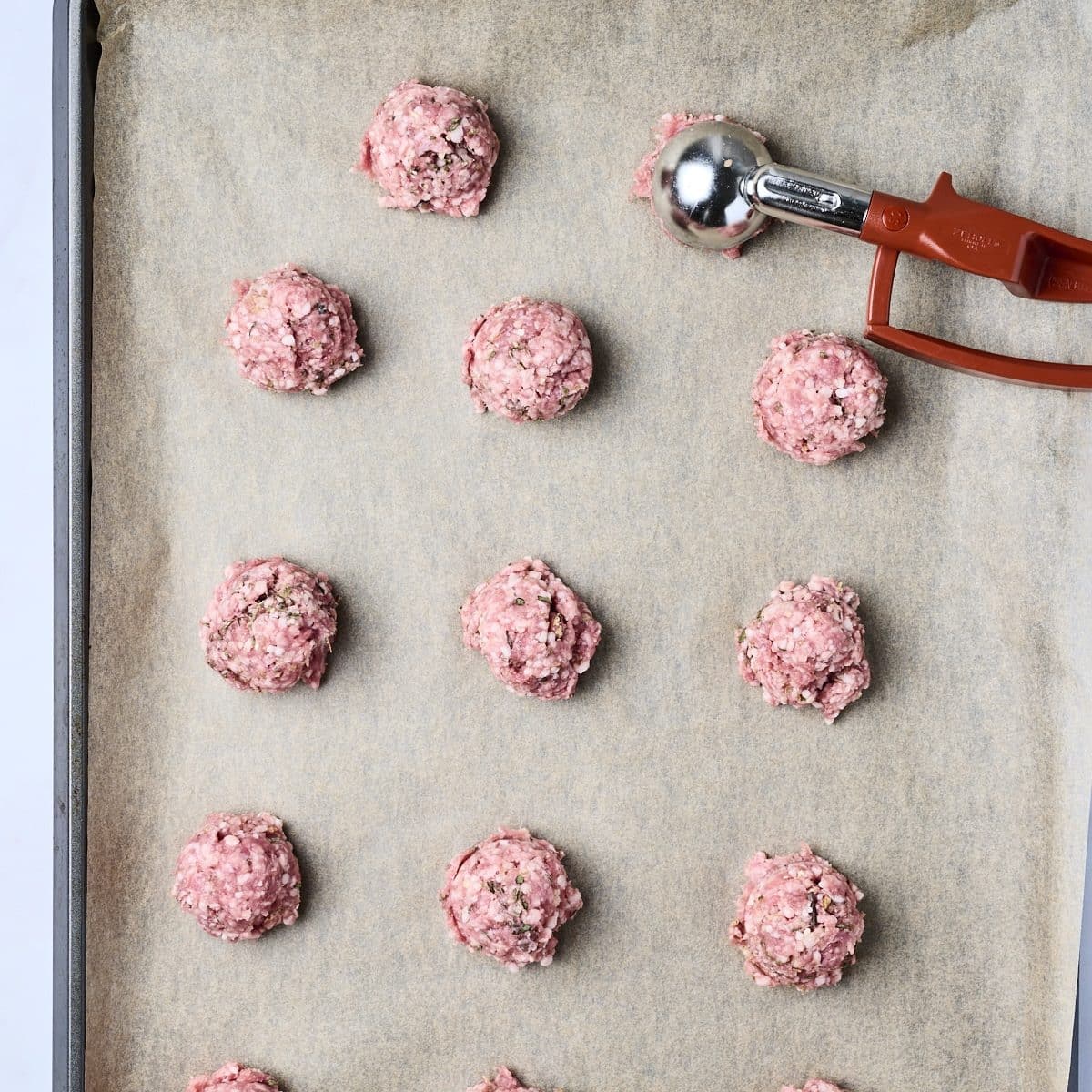 Uncooked lamb meatballs on a baking sheet lined with parchment paper