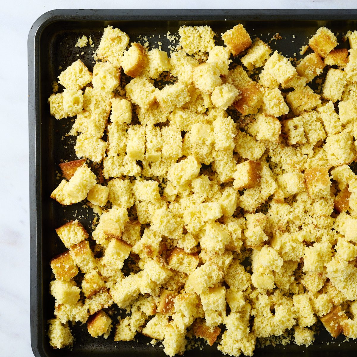 Cornbread cubes on a dark baking pan. 