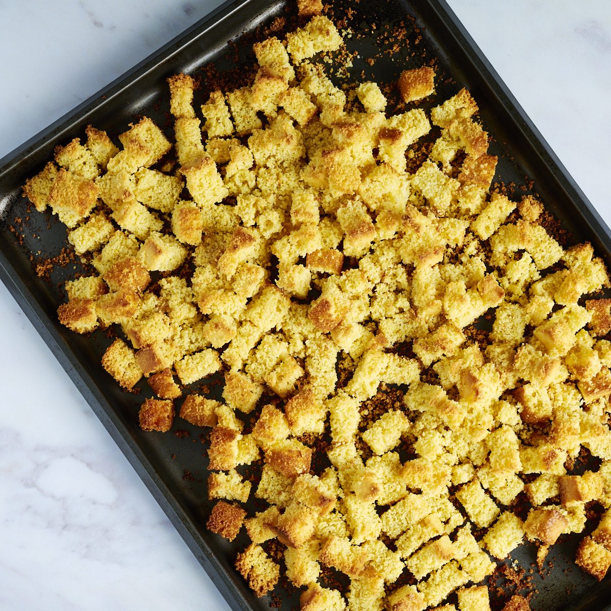 Toasted cornbread cubes on a dark baking sheet