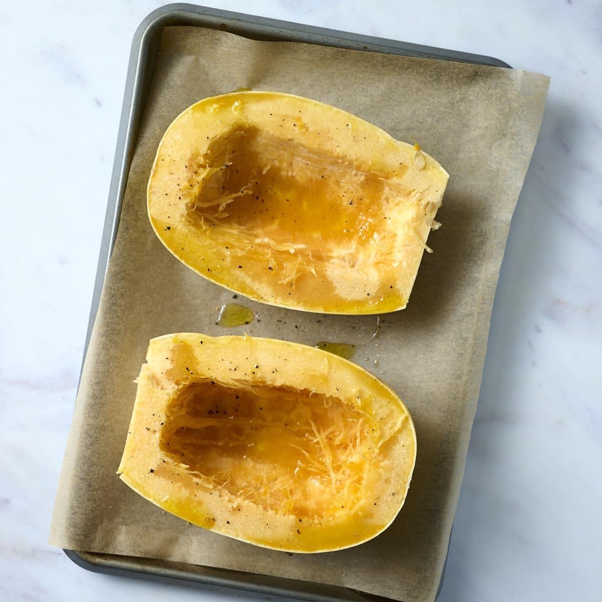 Two spaghetti squash halves on a baking sheet