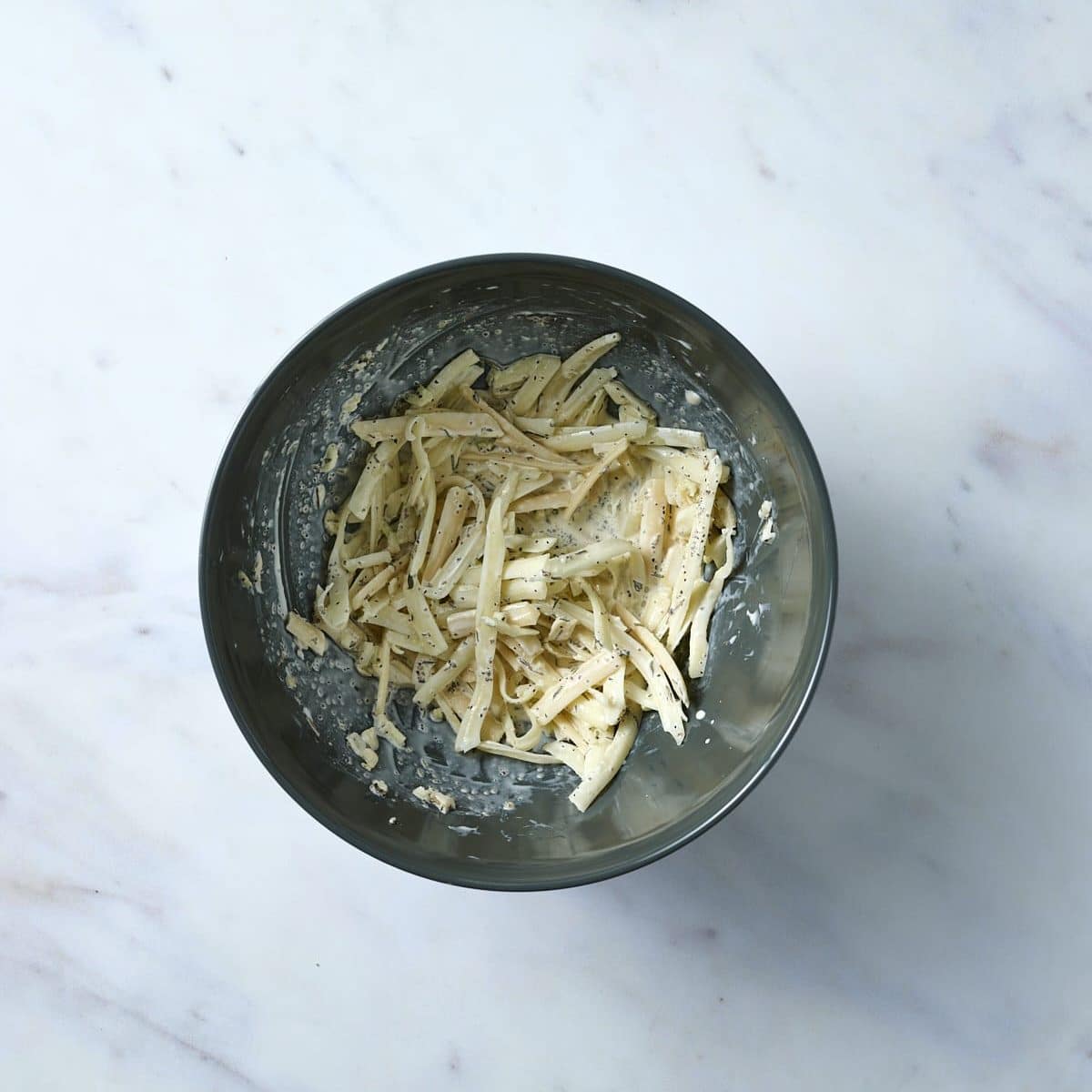 Italian cheese shreds in a dark bowl, mixed with cream & herb