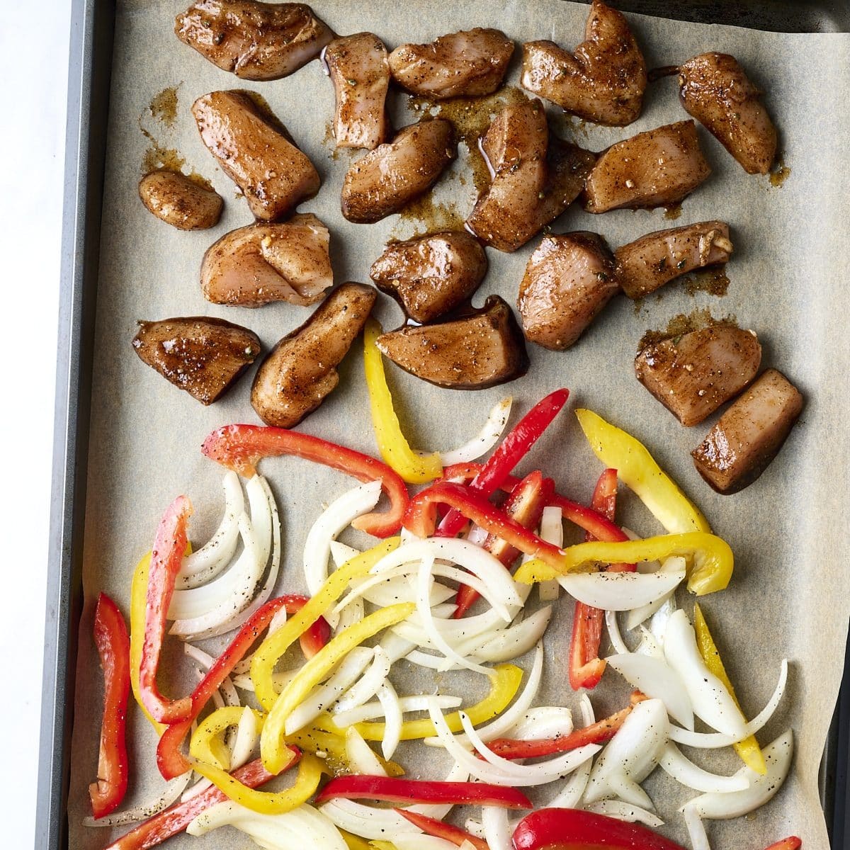 Sliced chicken and peppers for fajitas on a sheet pan