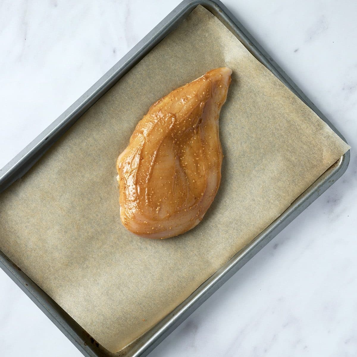 Chicken breast marinated in peanut sauce on a baking sheet