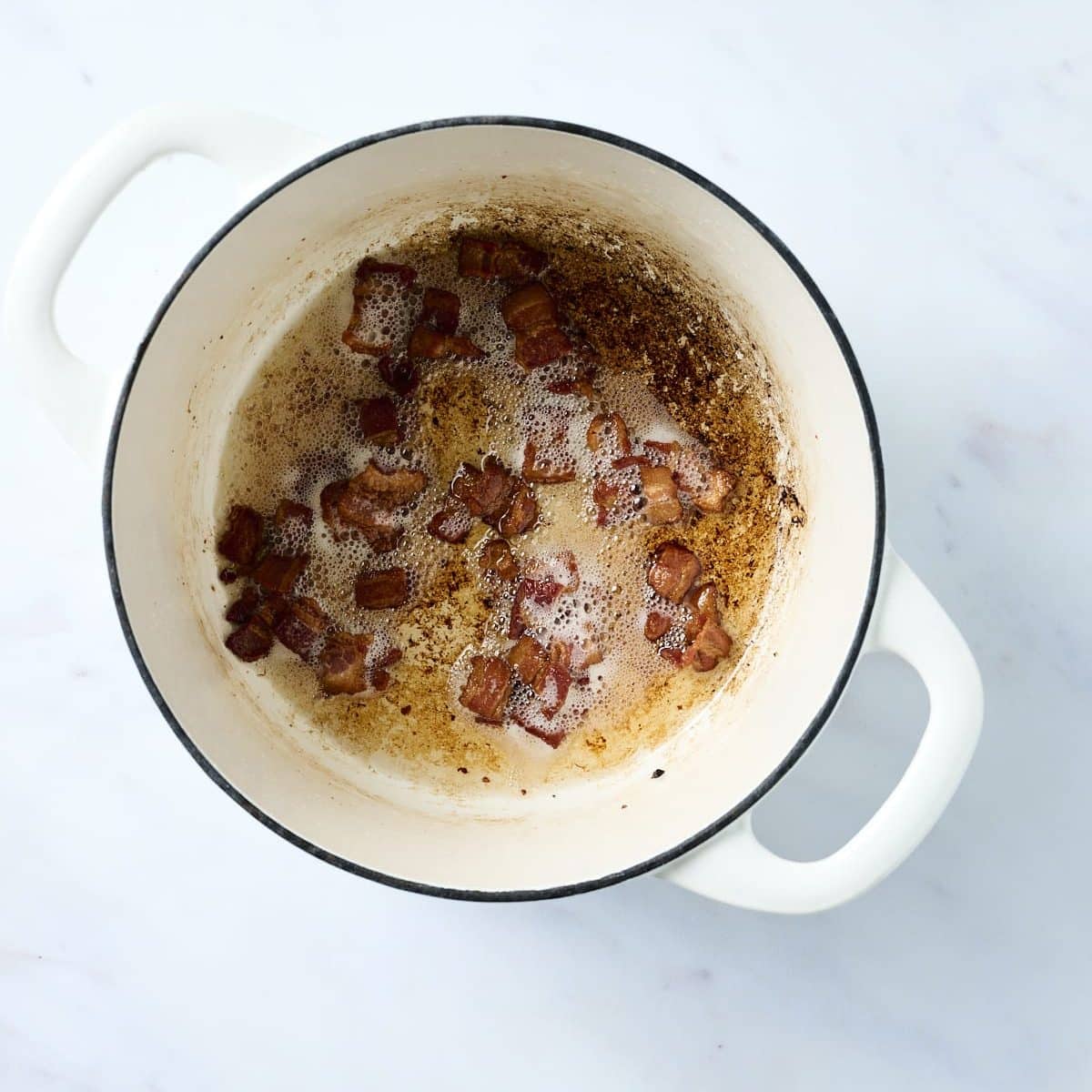 Chopped bacon cooking in a small white dutch oven