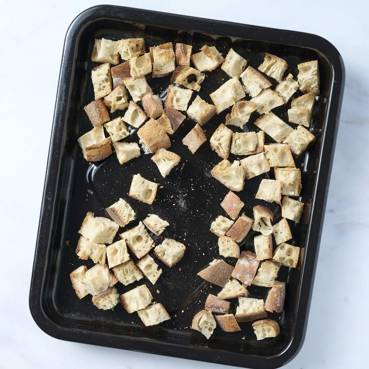 Toasted bread cubes on a black baking pan