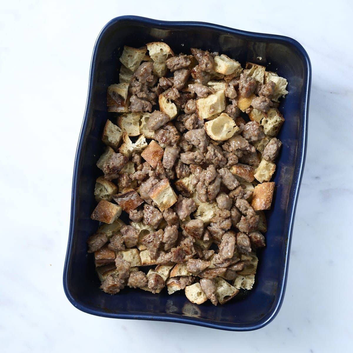 Blue baking dish filled with bread cubes and sausage for breakfast casserole