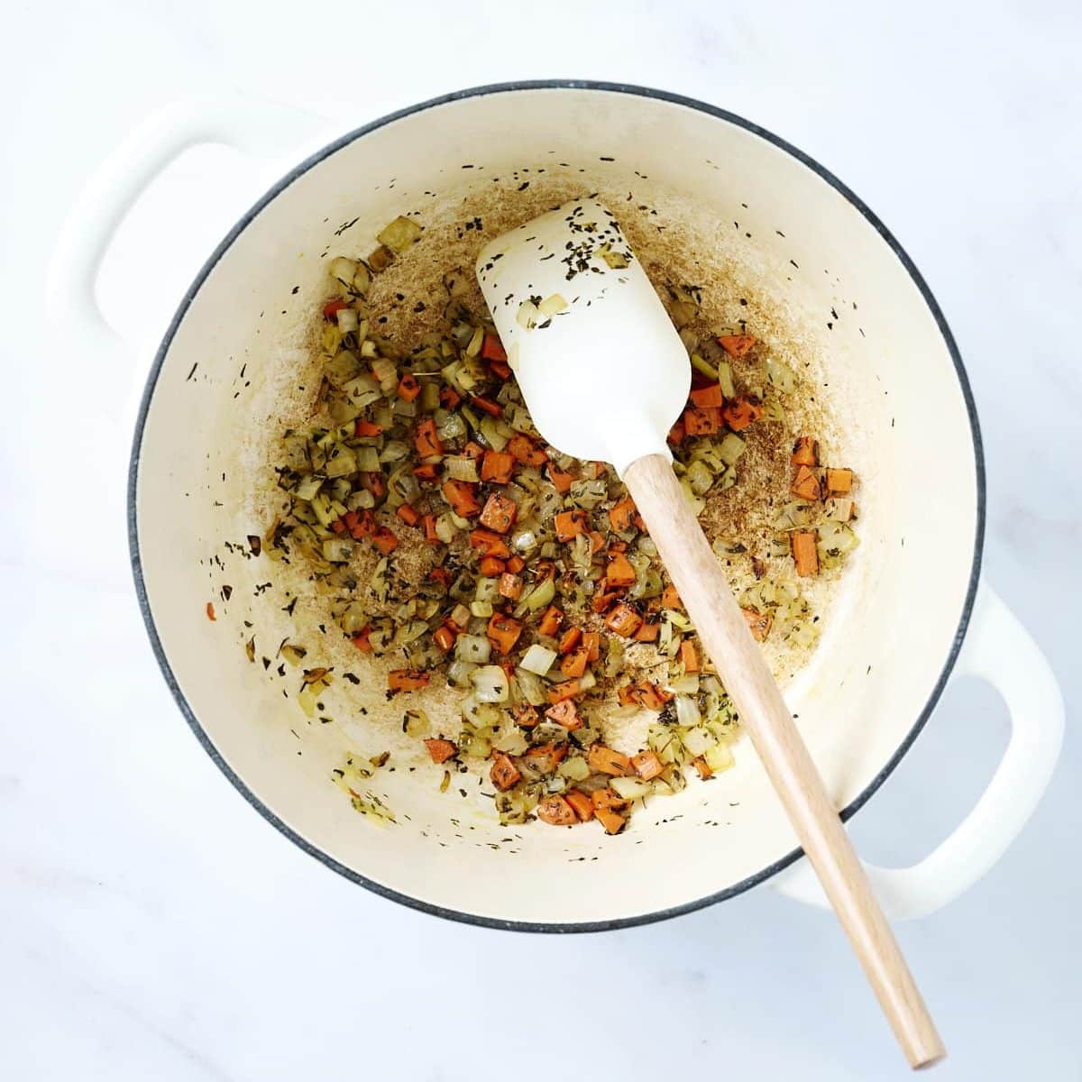 White dutch oven with carrots and onions for tomato soup base
