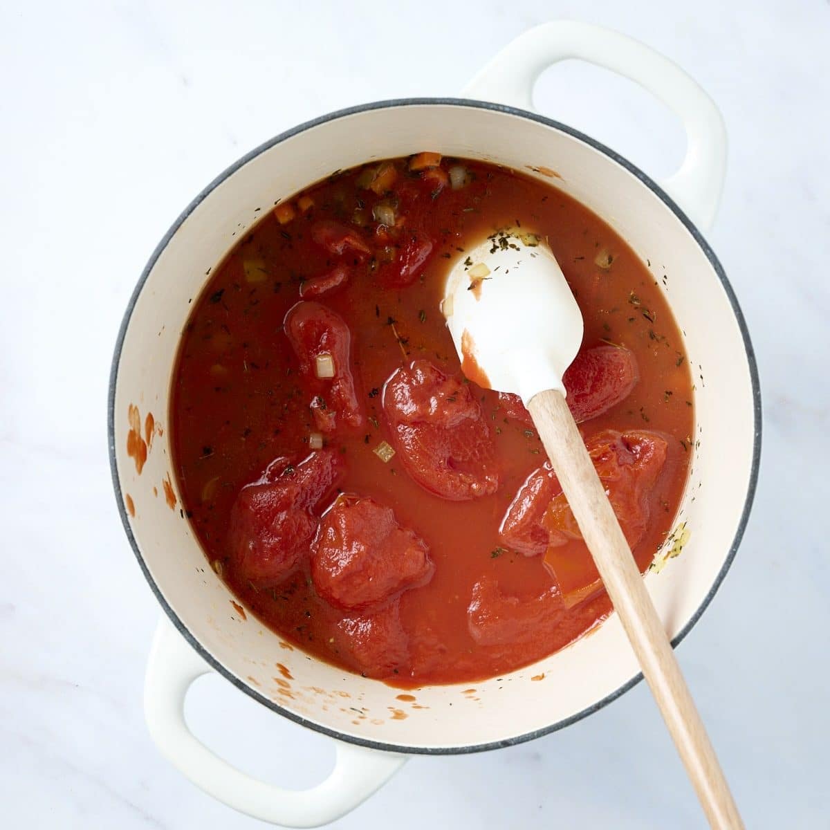 Whole tomatoes cooking in white dutch oven