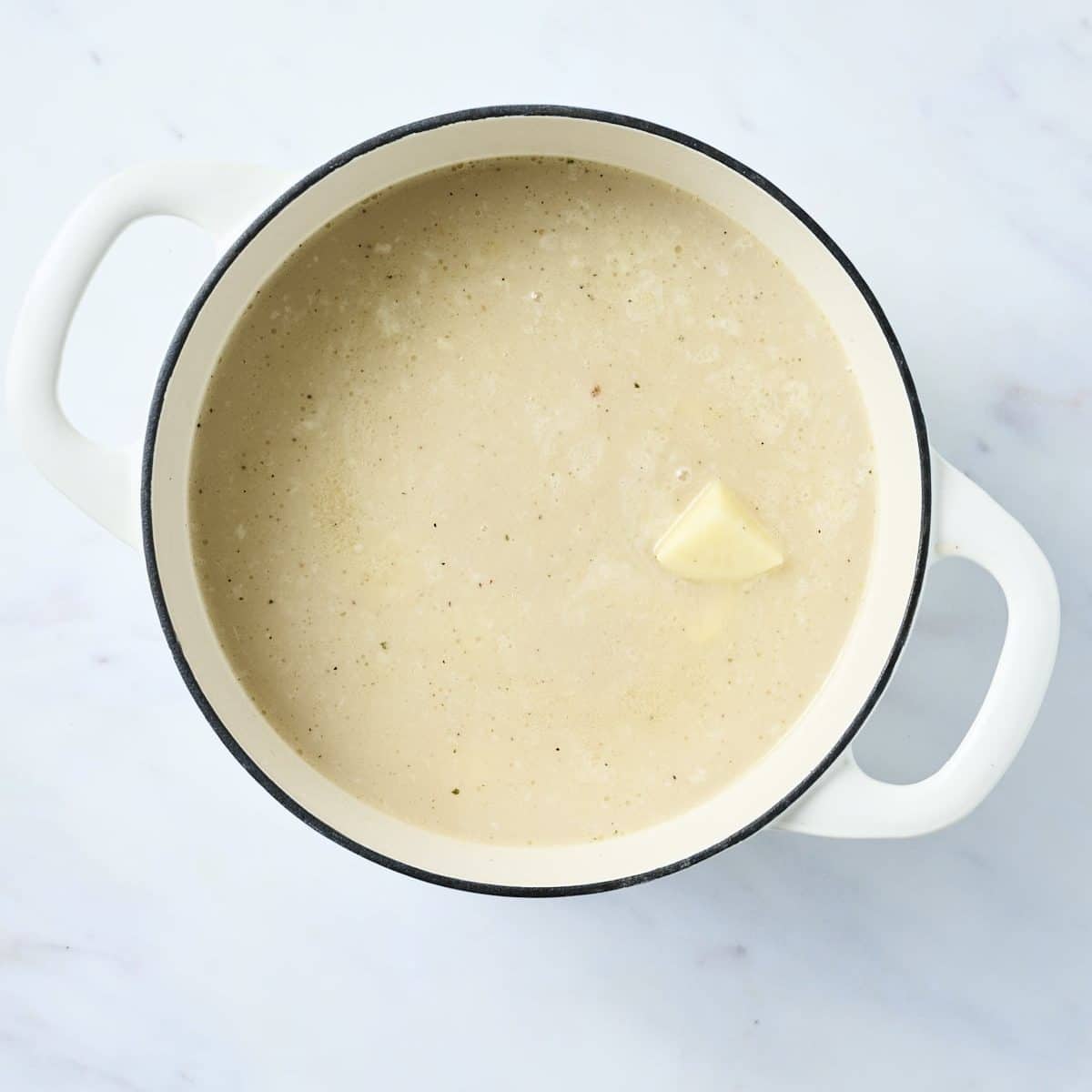 Chicken broth base and chopped potatoes for baked potato soup in a white dutch oven