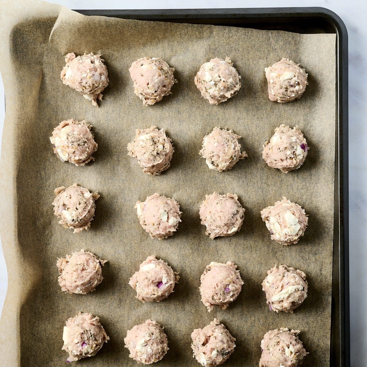 Uncooked chicken meatballs on a baking sheet