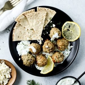 Overhead shot of chicken meatballs, tzatziki sauce and lemon slices on a black plate