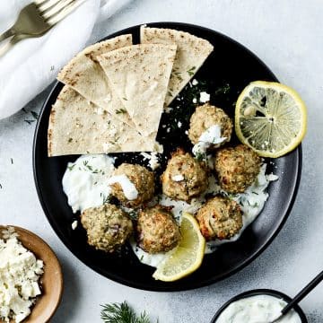 Overhead shot of chicken meatballs, tzatziki sauce and lemon slices on a black plate