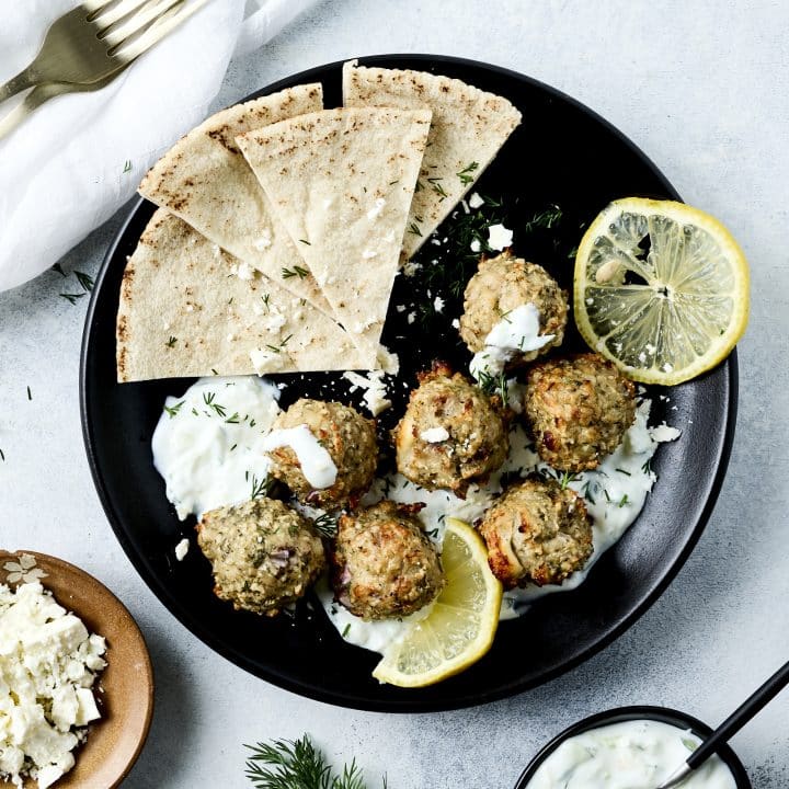 Overhead shot of chicken meatballs, tzatziki sauce and lemon slices on a black plate