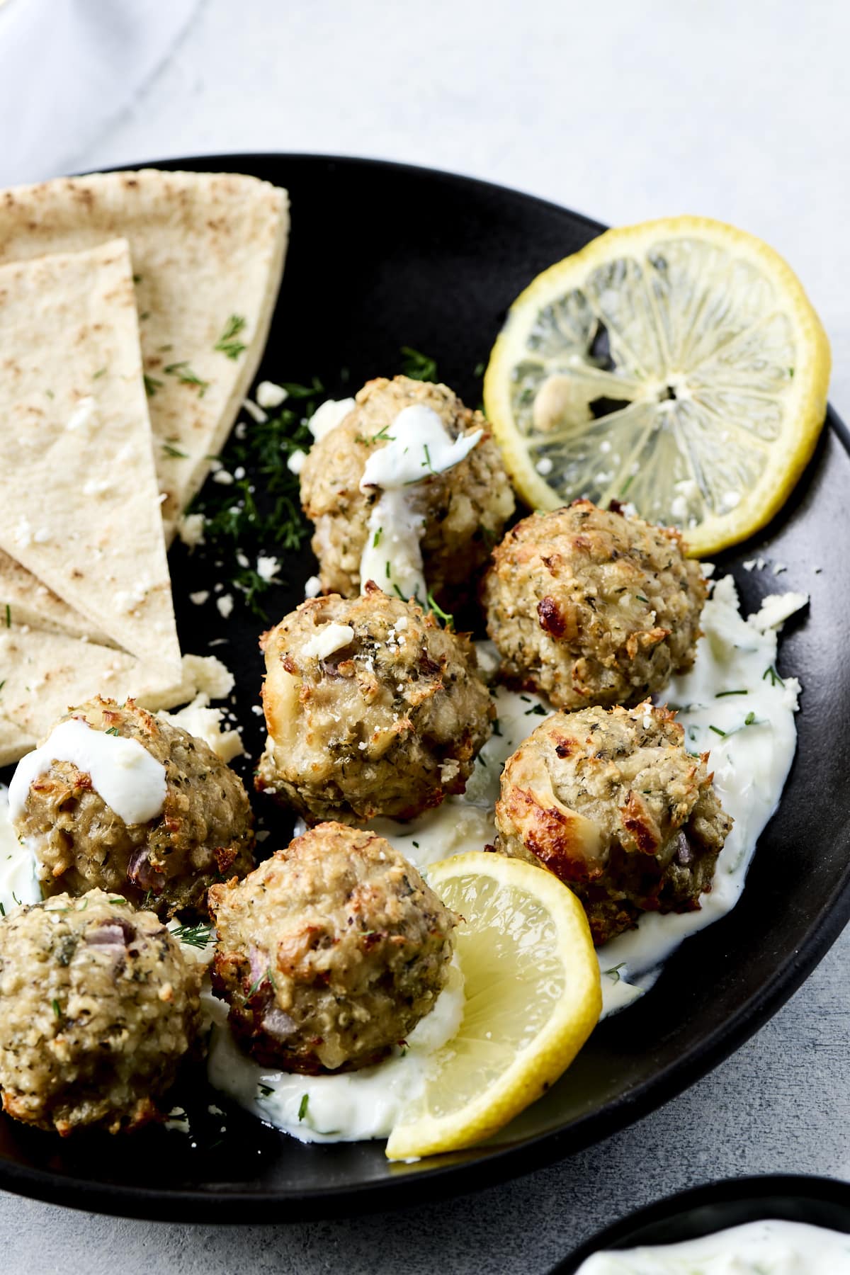 Close up of chicken meatballs and tzatziki sauce on a matte black plate