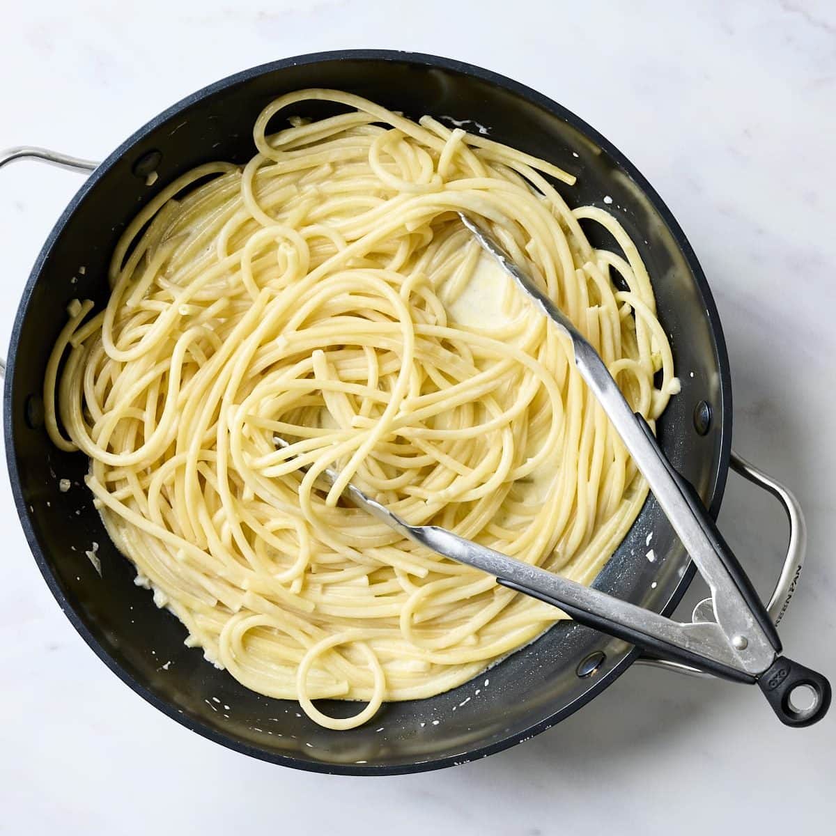 Bucatini pasta in a pan with creamy lemon sauce.