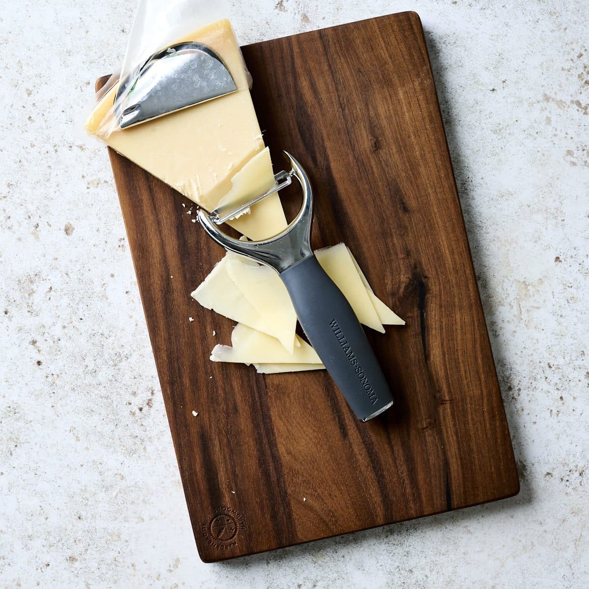 Wedge of parmesan cheese on a cutting board with a peeler