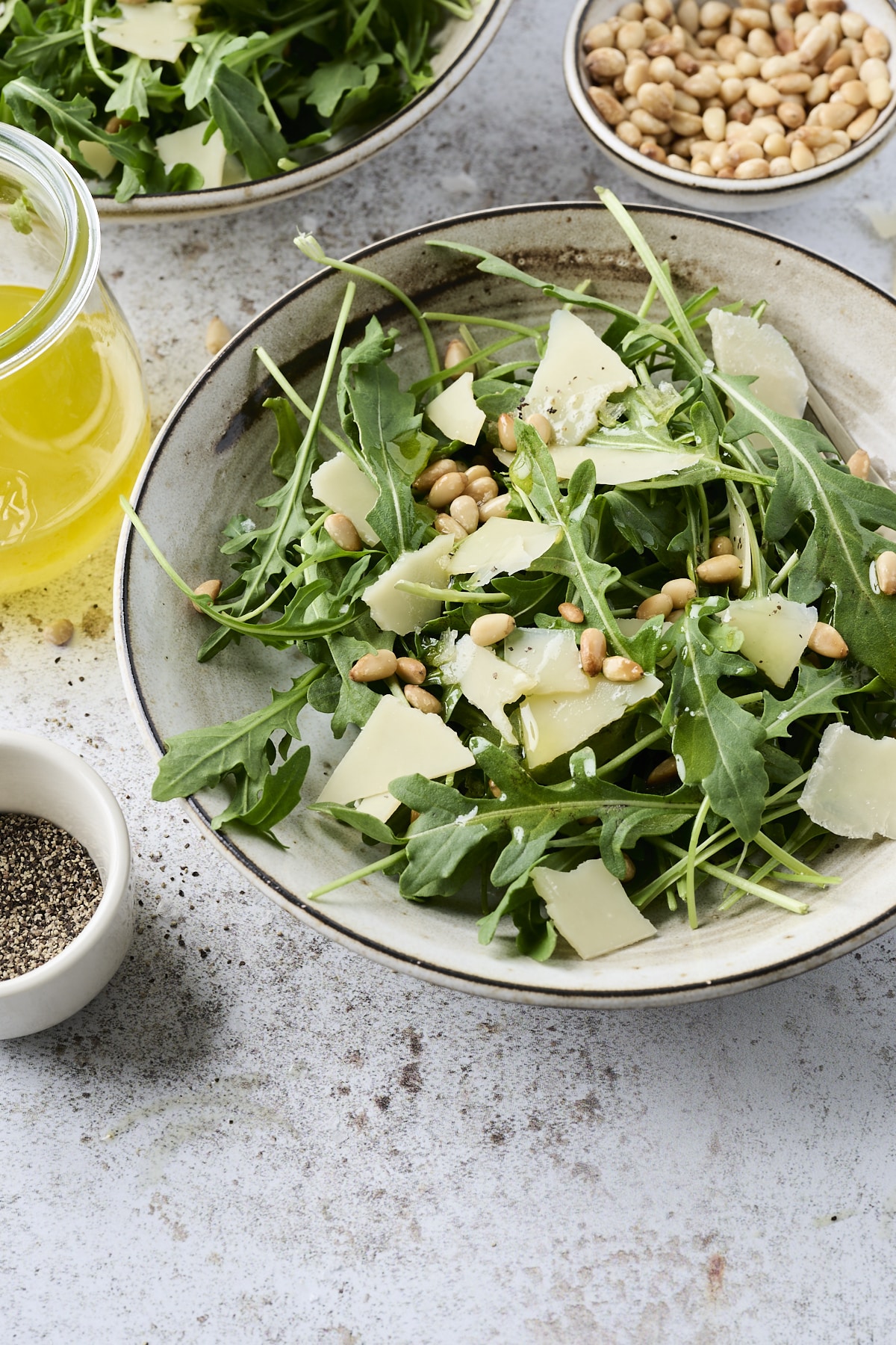 Two small bowls with arugula topped with toasted pine nuts and shaved parmesan