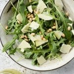 Small salad bowl filled with arugula topped with pine nuts and shaved parmesan cheese