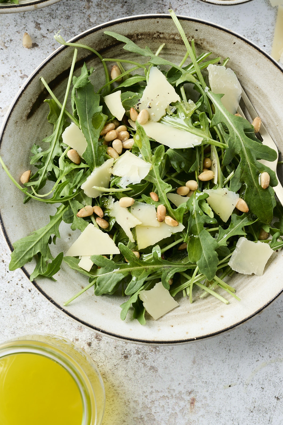 Small salad bowl filled with arugula topped with pine nuts and shaved parmesan cheese