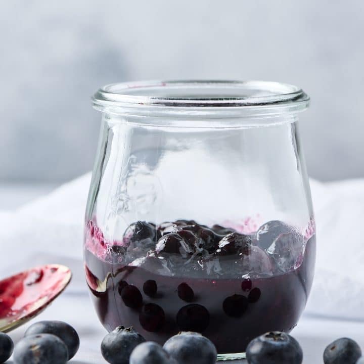 Blueberry compote in a small glass jar with fresh blueberries in front of it