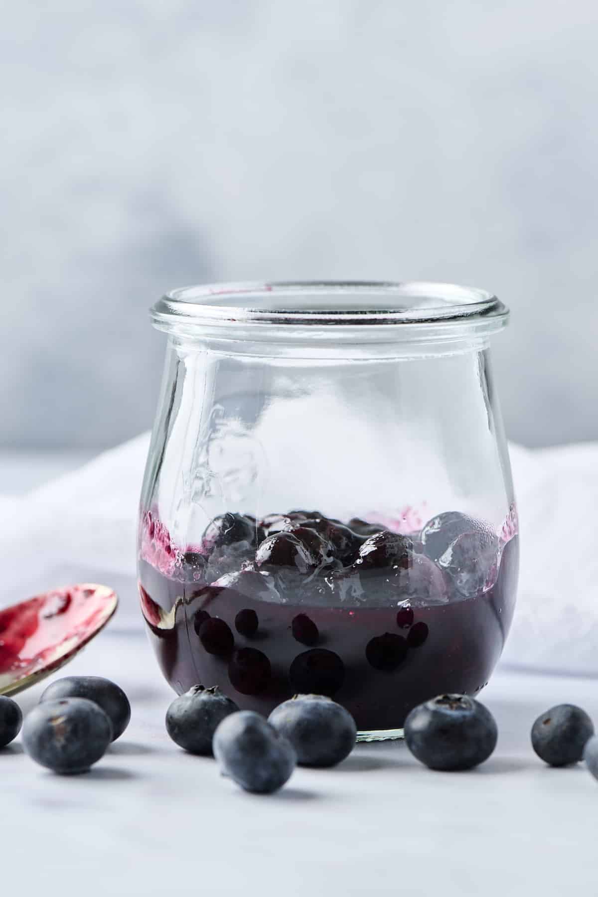 Blueberry compote in a small glass jar with fresh blueberries in front of it