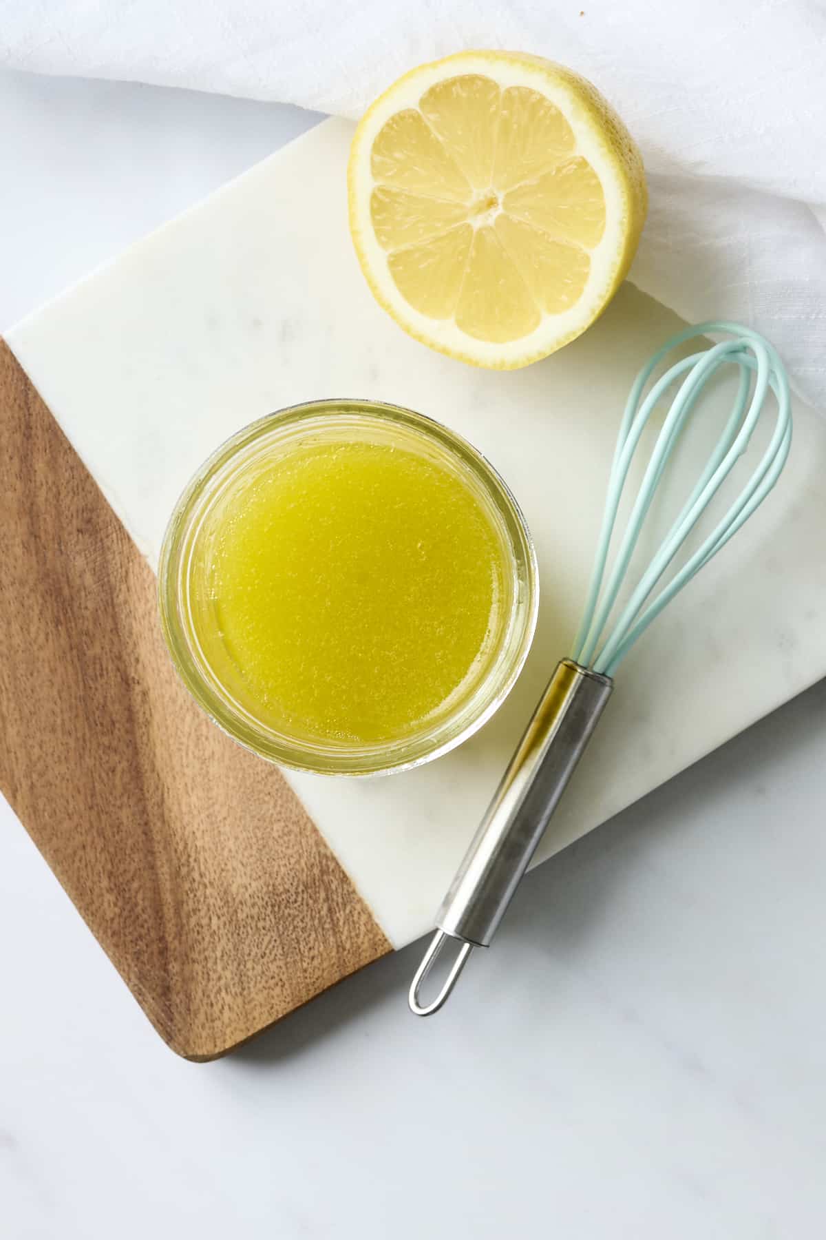 Bowl filled with lemon vinaigrette and half of a lemon on a cutting board