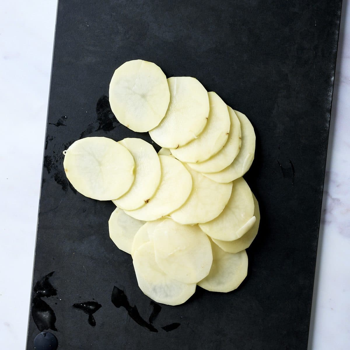 Potatoes sliced with a mandoline on a black cutting board