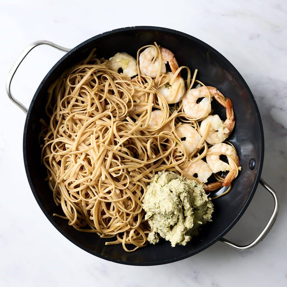 Linguine, artichoke pesto and cooked shrimp in a large sauté pan