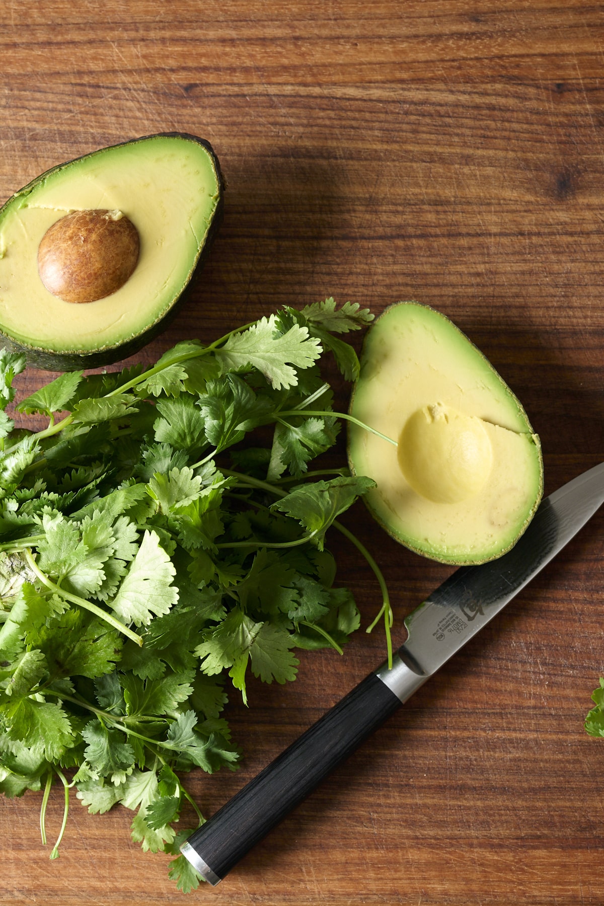 Halved avocado and cilantro on a brown cutting board