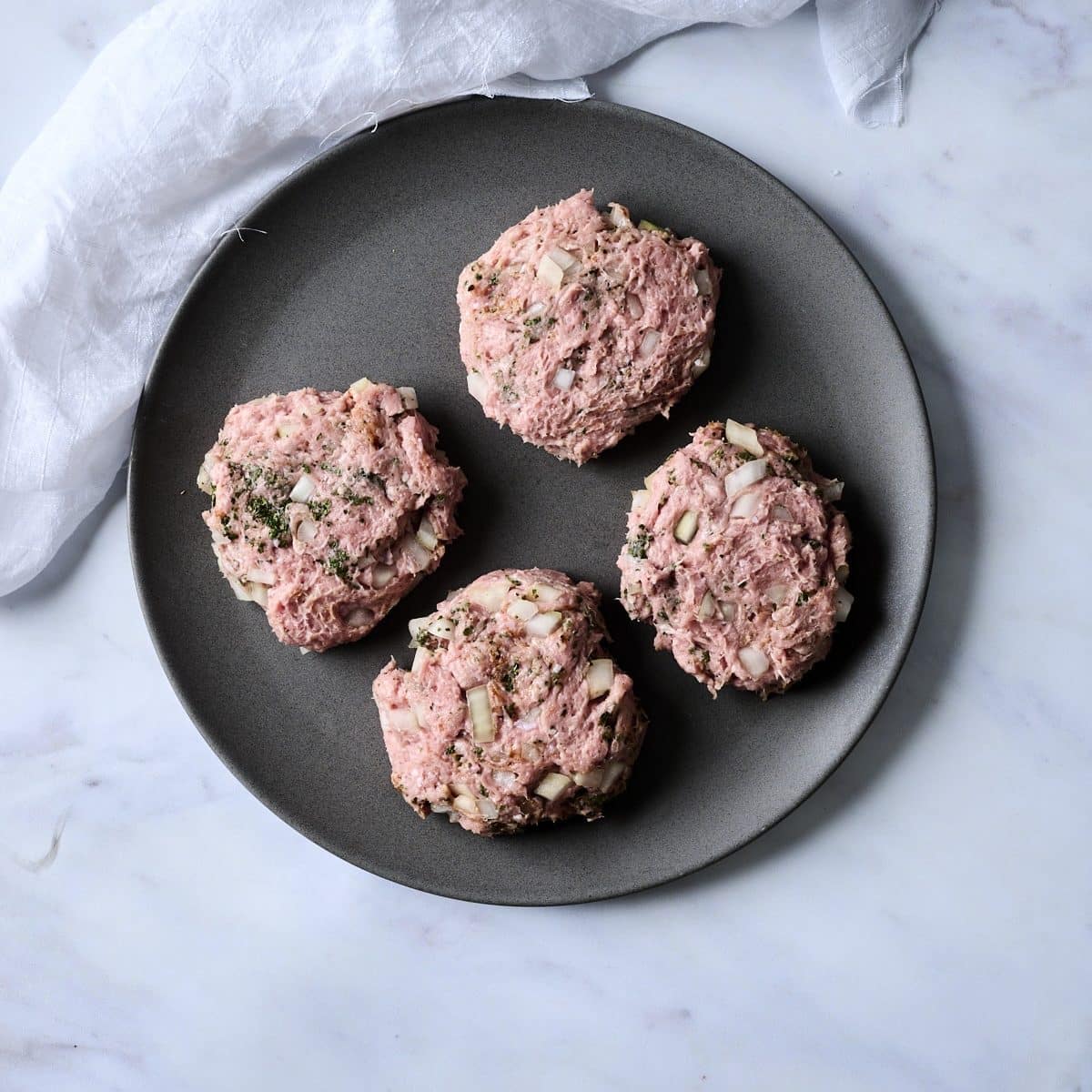 Uncooked turkey burgers on a dark grey plate