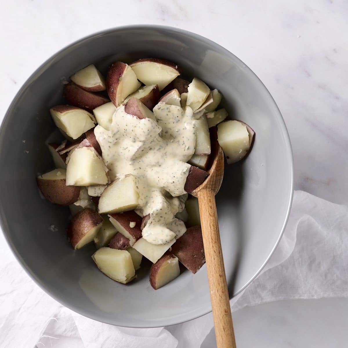 Chopped boiled potatoes topped with dressing in a grey bowl